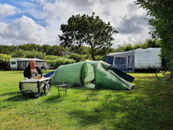Kleines Zelt auf Campingplatz, mit einer davor sitzenden Frau