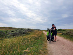 Frau mit bepacktem Fahrrad in der dänischen Dünenlandschaft