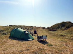 Kleines Zelt, ein Fahrradanhänger und eine Frau in den dänischen Dünen