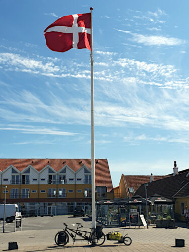 Bepacktes Tandem mit Anhänger, geparkt an einem hohen Fahnenmast, an dem die dänische Flagge weht