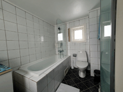 Blick in ein kleines, älteres Badezimmer mit Badewanne und Toilette.